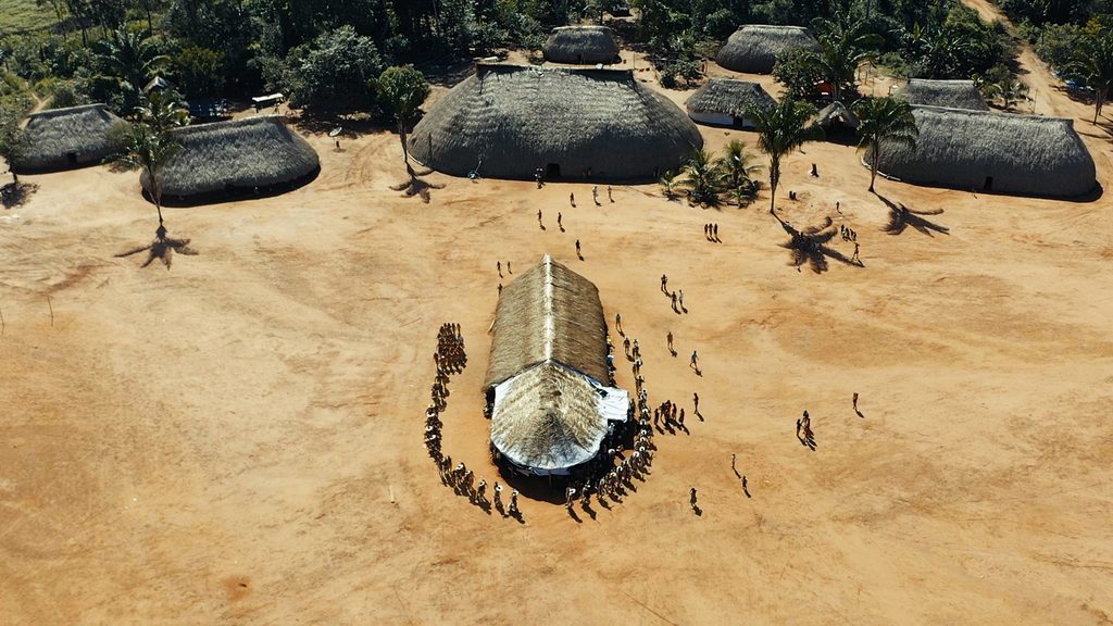 Vista aérea da aldeia em festa, Aldeia Moygu, Parque Indígena do Xingu. Cena do filme "Elas nunca vão andar sozinhas", em comemoração dos 10 anos do Movimento das Mulheres Yarang (MMY), que produz e coleta sementes nativas para o reflorestamento das nascentes e matas ciliares da bacia do rio Xingu no entorno do TIX. Direção de Fernanda Ligabue/ISA e realização do Movimento das Mulheres Yarang, Associação Rede de Sementes do Xingu e Associação Indígena Moygu Comunidade Ikpeng @file:///home/alex/Desktop/Xingu