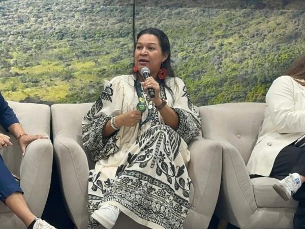 Cristiane Julião aparece sentada em uma poltrona palestrando