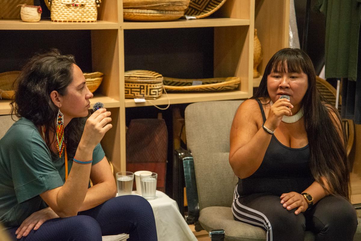 A liderança indígena Yakuwipu Waurá fala ao microfone, sentada ao lado de  Karina Araujo, analista de desenvolvimento de pesquisa social do ISA