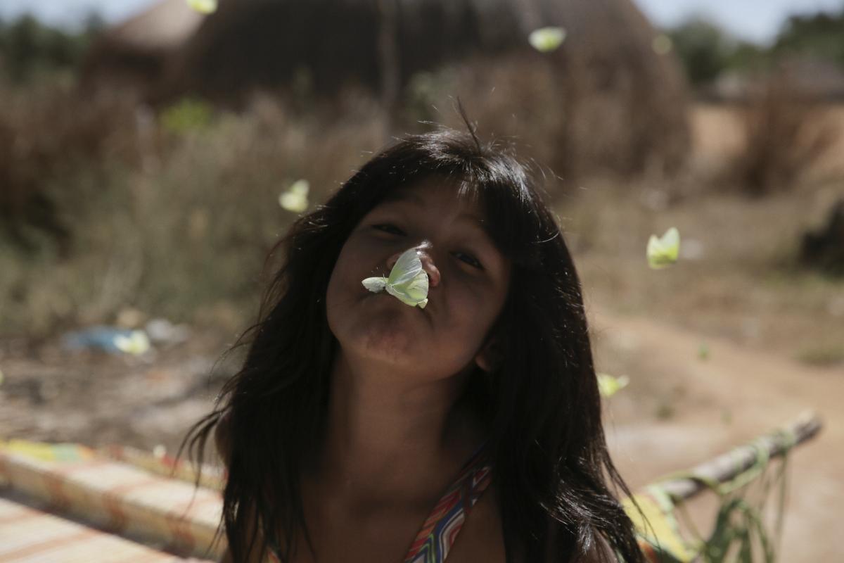Jepi Kaiulu Kalapalo brinca alegremente com borboletas em frente à sua casa. Na Aldeia Kalapalo, Terra Indígena do Xingu, o mês de abril é o período em que esses pequenos e belos insetos são abundantes e proporcionam às crianças momentos de diversão e encantamento