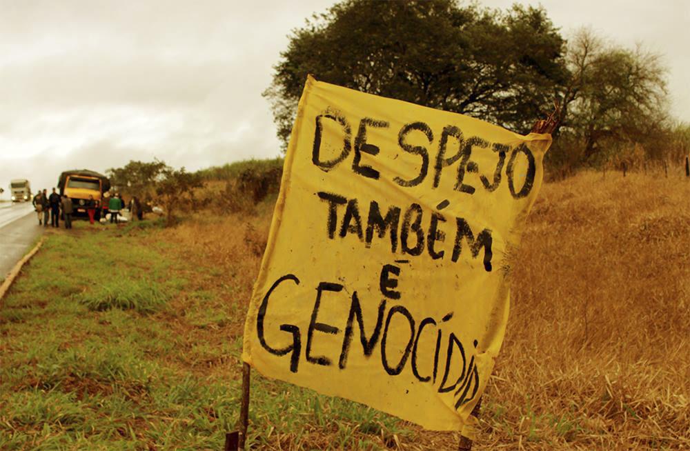 Cartaz em beira de estrada tem a seguinte frase escrita "despejo também é genocida"