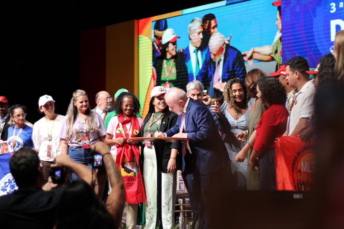 Presidente Lula assina documento em púlpito, rodeado por lideranças quilombolas e outros integrantes do governo