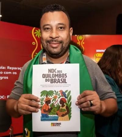 Foto mostra Biko Rodrigues segurando o material NDC Quilombola