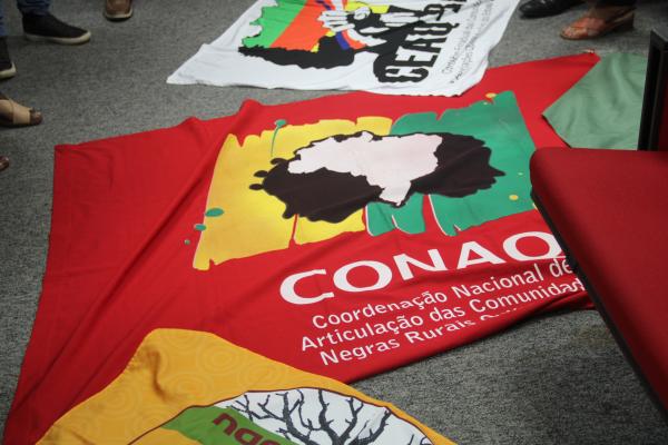 Bandeira da Conaq colocada à frente da mesa de coordenação da reunião da mesa de diálogo em protesto | Pedro Garcês / Conaq